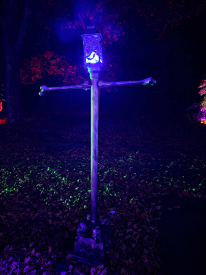 A streetlight or light post lit with blue fire effect. It's base is covered in skulls, the lamp has bats on it. 