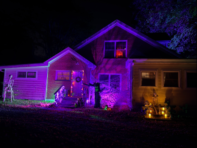 A Halloween scene with a skeletal Centaur, spooky tree, skeletons and pumpkins. There is a door with a wreath. There are steps leading to nowhere with creepy statues and a skeleton lit with candles. The scene is is veru colorfully lit.