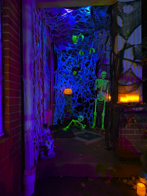 A Halloween porch with spider webs, glowing green skeletons and a glowing jack-o-lantern.