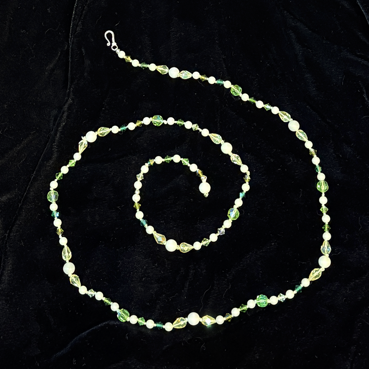 View of the necklace coiled to show the hook and tail clasp.This is a necklace I made with some of the leftover beads from my Green Fairy Halloween prop project (https://spoopylvania.com/GreenFairy). Her jewelry is adjustable so also made to be worn by me. This delicate necklace is made of quality vintage crystal, 'moon pearls' which are glow in the dark stone, vintage glass beads, and some Vaseline glass / uranium glass in various greens, soft white, and pale yellow. It is hand knotted between each bead. It glows like crazy in blacklight and glows in the dark but looks beautiful with lots of sparkle in regular light too. The length is 28 inches from end to end and is adjustable with a hook and tail clasp. It can be worn as a choker or  longer.