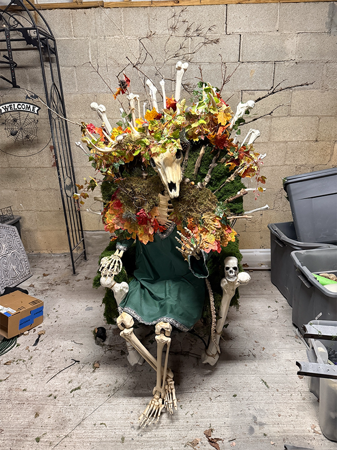 A forest god with a deer skull sits on a throne made of bones and moss and leaves.