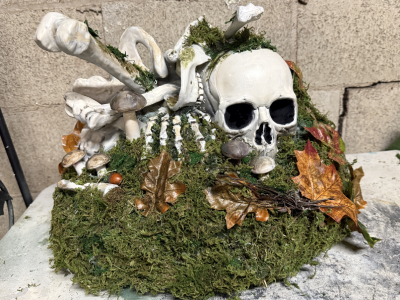 a mossy bone pile with mushrooms and leaves sitting on a table in front of a cinder block wall.